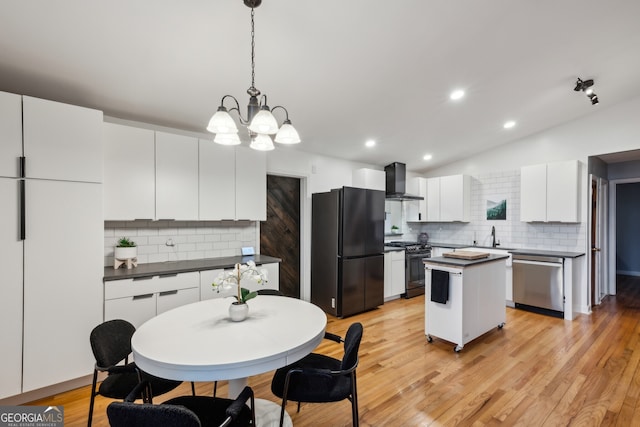 kitchen featuring wall chimney range hood, freestanding refrigerator, dishwasher, dark countertops, and gas range