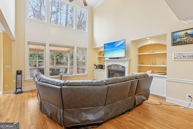 living room with a premium fireplace, a healthy amount of sunlight, built in features, and light wood-type flooring