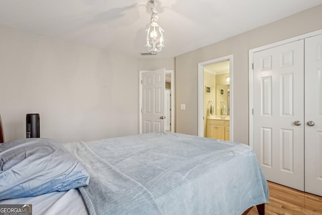 bedroom with hardwood / wood-style flooring, ensuite bathroom, an inviting chandelier, and a closet