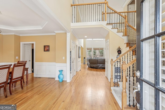 foyer featuring a high ceiling, ornamental molding, and light hardwood / wood-style flooring