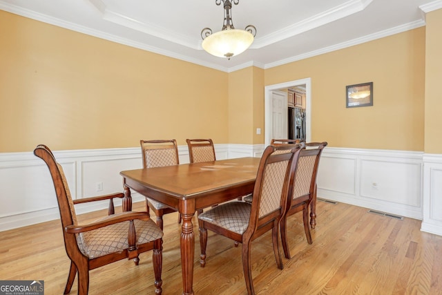 dining area with crown molding, a raised ceiling, and light hardwood / wood-style floors