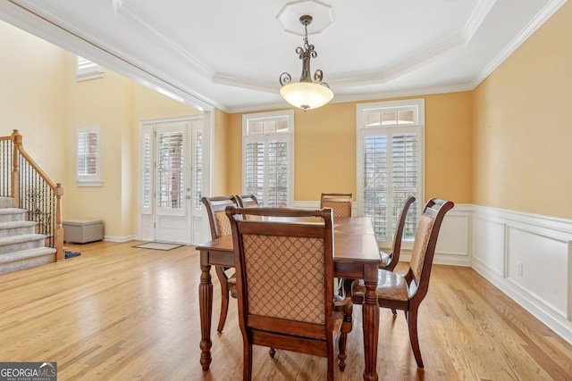 dining room with crown molding, a tray ceiling, and light hardwood / wood-style flooring