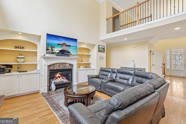 living room with a premium fireplace, ornamental molding, light wood-type flooring, and built in shelves