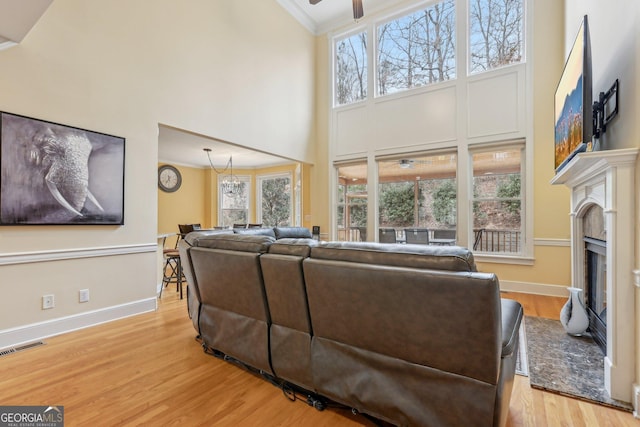 living room featuring crown molding, ceiling fan, light hardwood / wood-style flooring, and a towering ceiling