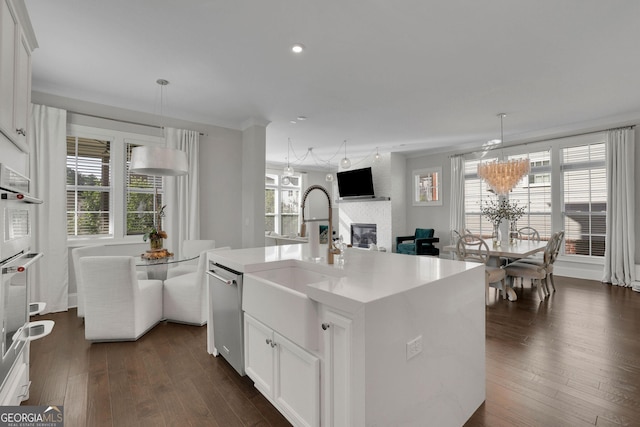 kitchen with white cabinetry, stainless steel appliances, a kitchen island with sink, and hanging light fixtures