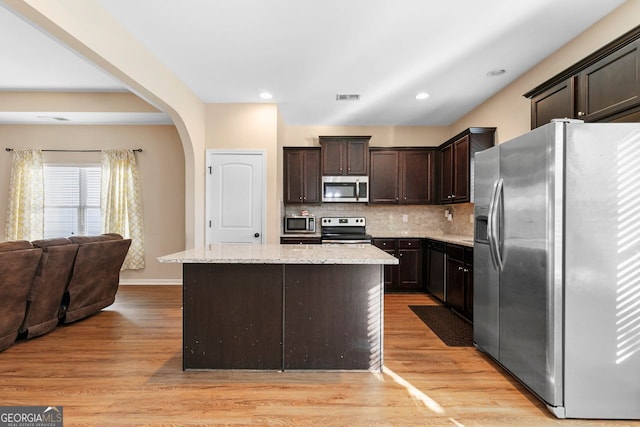 kitchen featuring appliances with stainless steel finishes, dark brown cabinets, decorative backsplash, light hardwood / wood-style floors, and a center island