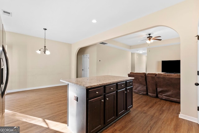 kitchen featuring a center island, dark brown cabinetry, light stone counters, hardwood / wood-style floors, and pendant lighting