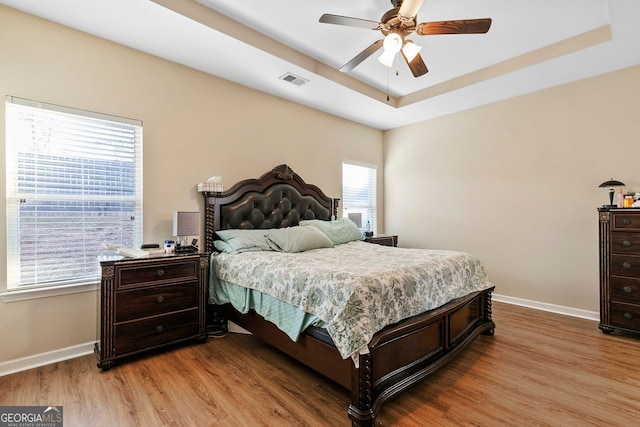 bedroom with light wood-type flooring, a tray ceiling, and ceiling fan