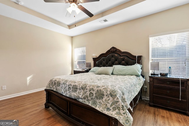 bedroom with a raised ceiling, ceiling fan, and wood-type flooring