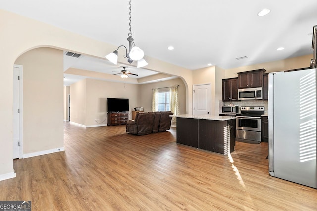 kitchen featuring stainless steel appliances, dark brown cabinetry, decorative light fixtures, light hardwood / wood-style flooring, and a center island
