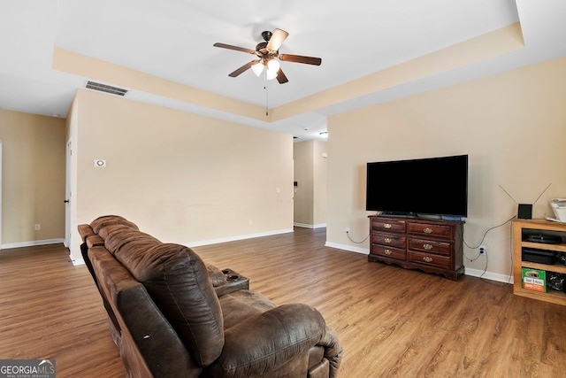 living room featuring ceiling fan, light hardwood / wood-style floors, and a raised ceiling