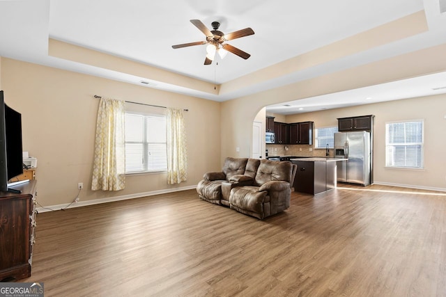 living room with light wood-type flooring, ceiling fan, and a raised ceiling