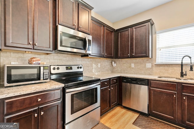 kitchen with sink, light stone counters, stainless steel appliances, and dark brown cabinetry