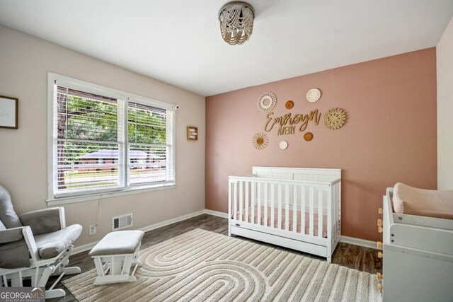 bedroom with dark wood-type flooring and a nursery area