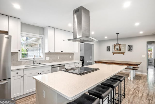 kitchen with pendant lighting, sink, white cabinets, island exhaust hood, and stainless steel appliances