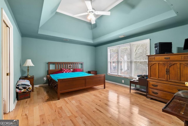 bedroom featuring ceiling fan, a tray ceiling, light wood-type flooring, and baseboards