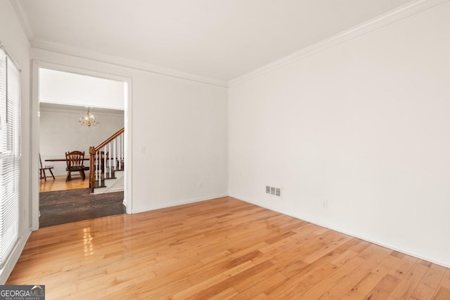 empty room with a chandelier, wood finished floors, visible vents, stairs, and ornamental molding