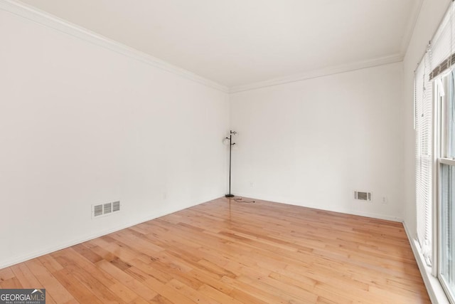 empty room with light wood-style flooring, visible vents, and ornamental molding