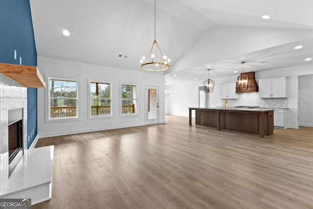 unfurnished living room featuring high vaulted ceiling, a high end fireplace, a chandelier, and light hardwood / wood-style floors