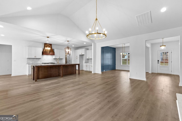 kitchen with white cabinetry, decorative backsplash, hanging light fixtures, a kitchen island with sink, and an inviting chandelier