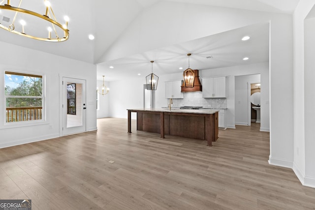 kitchen featuring a chandelier, light hardwood / wood-style flooring, hanging light fixtures, a kitchen island with sink, and white cabinets