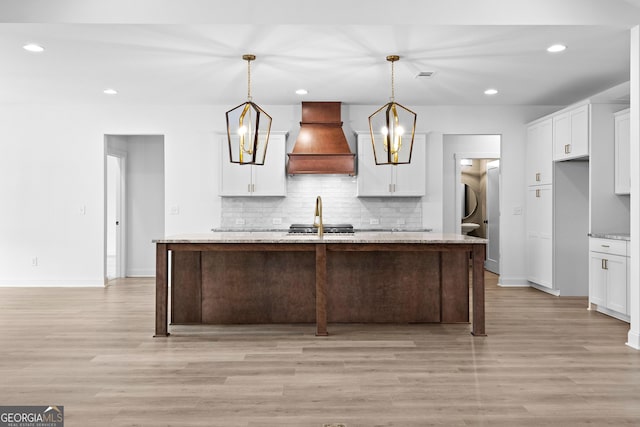 kitchen featuring pendant lighting, white cabinetry, custom exhaust hood, light stone counters, and a center island with sink