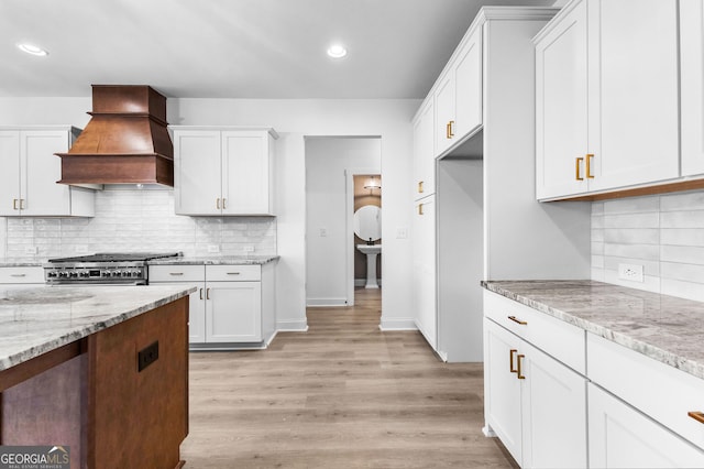 kitchen featuring white cabinetry, stainless steel stove, light stone countertops, and premium range hood