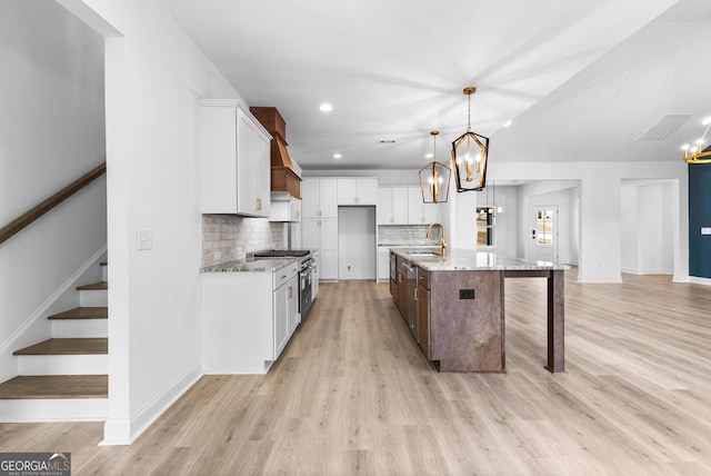 kitchen with high end stove, white cabinetry, an island with sink, hanging light fixtures, and light stone countertops