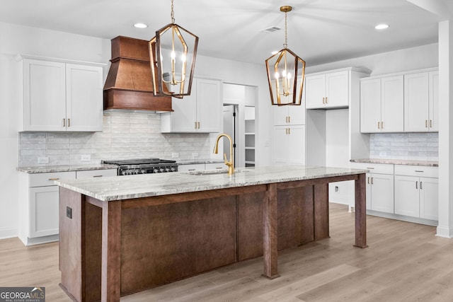 kitchen with custom exhaust hood, an island with sink, and white cabinets