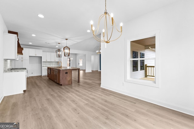 kitchen featuring light stone countertops, a kitchen island with sink, pendant lighting, and white cabinets