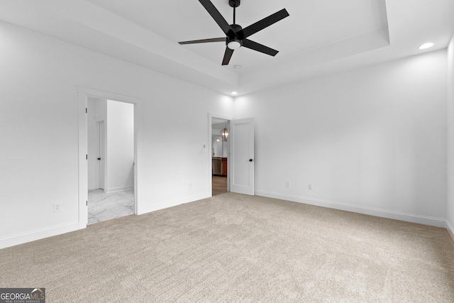 unfurnished bedroom featuring connected bathroom, light colored carpet, and a tray ceiling