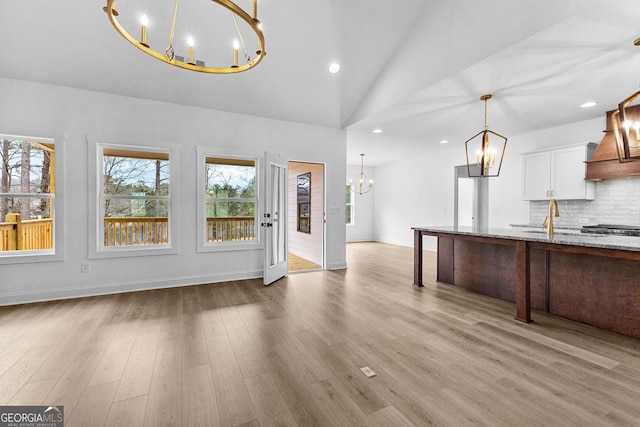 interior space featuring light stone counters, a notable chandelier, tasteful backsplash, white cabinets, and decorative light fixtures