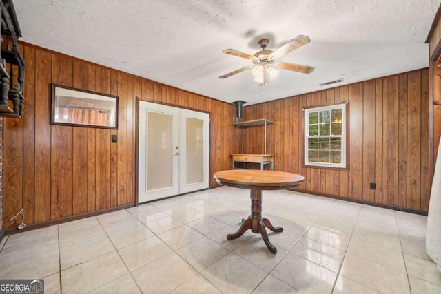 interior space with ceiling fan, wooden walls, french doors, and a textured ceiling