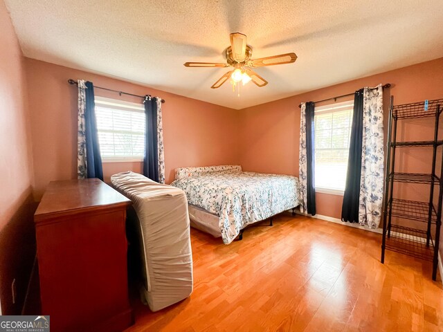 bedroom featuring ceiling fan, a textured ceiling, multiple windows, and light wood-type flooring