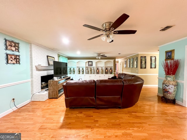 living room with crown molding, a brick fireplace, ceiling fan, and light hardwood / wood-style flooring