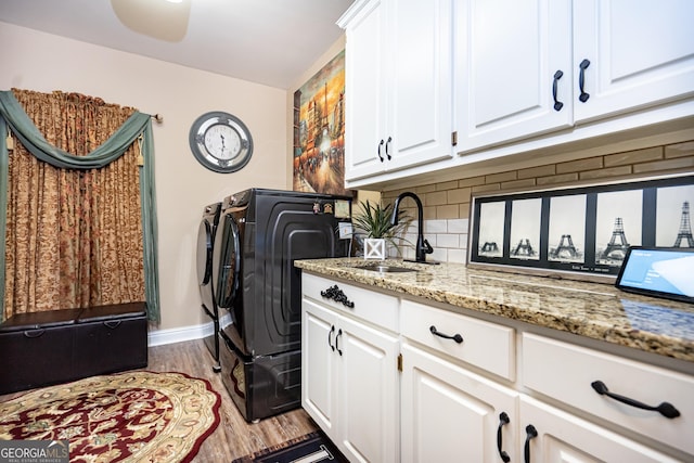 clothes washing area featuring cabinets, washing machine and clothes dryer, light hardwood / wood-style floors, and sink