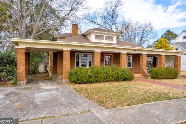 view of front of property with a chimney, brick siding, a front lawn, and driveway