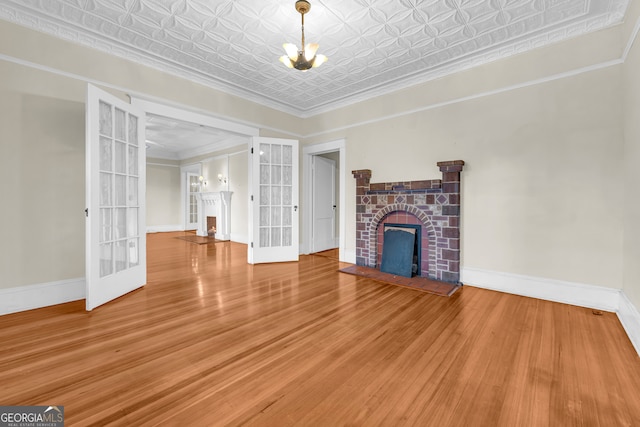 unfurnished living room with a fireplace with raised hearth, french doors, baseboards, an ornate ceiling, and a chandelier