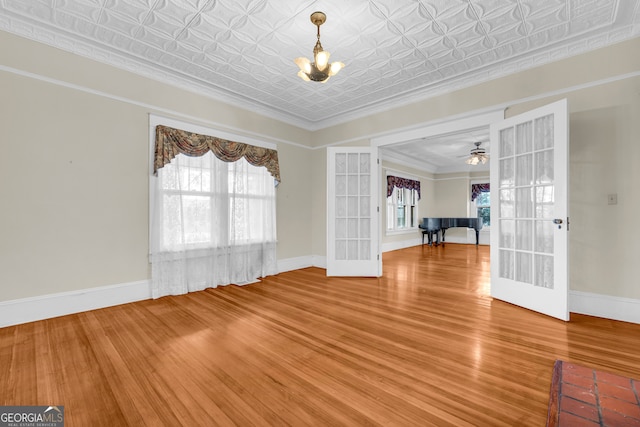 spare room with hardwood / wood-style floors, ceiling fan with notable chandelier, ornamental molding, and french doors