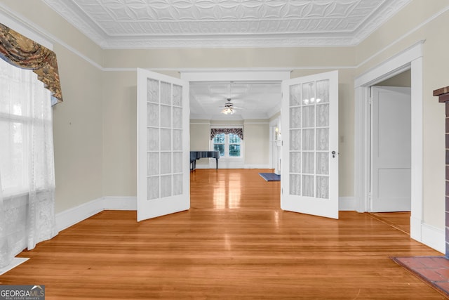 empty room featuring wood finished floors, french doors, baseboards, a ceiling fan, and ornamental molding