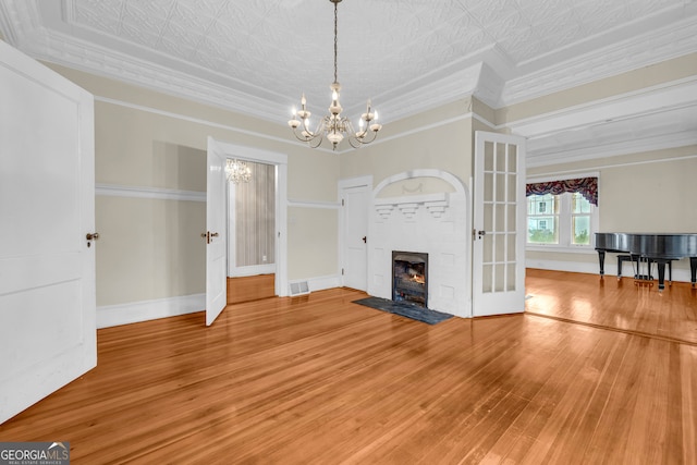 unfurnished living room featuring a tile fireplace, wood-type flooring, a notable chandelier, and ornamental molding