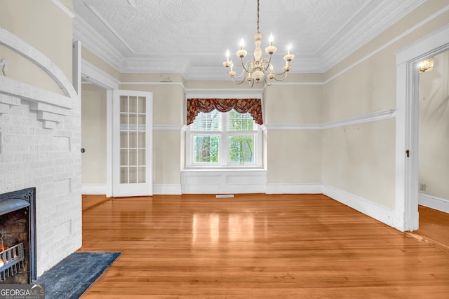 unfurnished dining area with wood finished floors, a chandelier, ornamental molding, and a stone fireplace