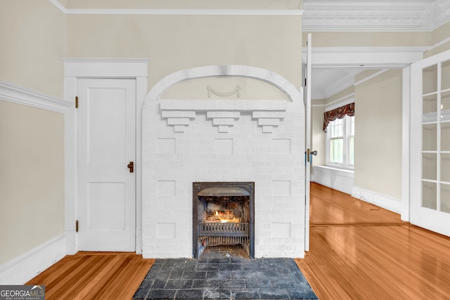detailed view of ornamental molding, wood finished floors, and a stone fireplace