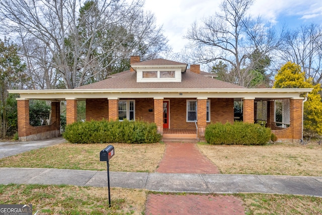 view of front facade featuring a chimney, a porch, brick siding, and a front yard