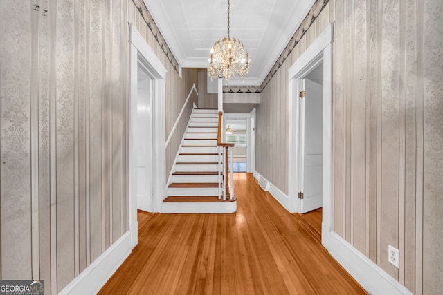 hallway featuring a chandelier, stairs, hardwood / wood-style floors, baseboards, and crown molding