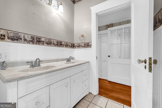 full bath featuring tile patterned floors, double vanity, and a wainscoted wall