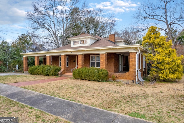 view of front of property featuring covered porch, brick siding, a front yard, and a shingled roof
