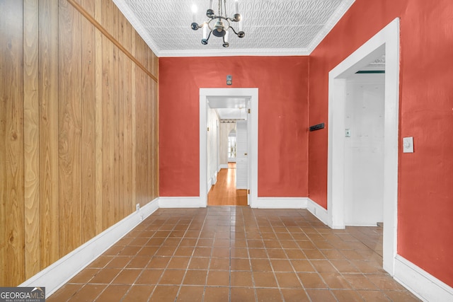 hall with an inviting chandelier, ornamental molding, wooden walls, and dark tile patterned floors