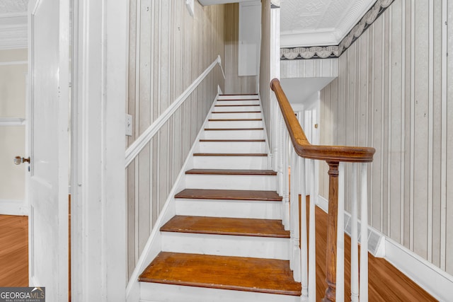 staircase featuring ornamental molding and wood walls