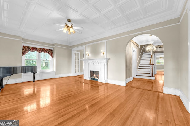 unfurnished living room featuring a ceiling fan, stairs, wood finished floors, arched walkways, and a fireplace